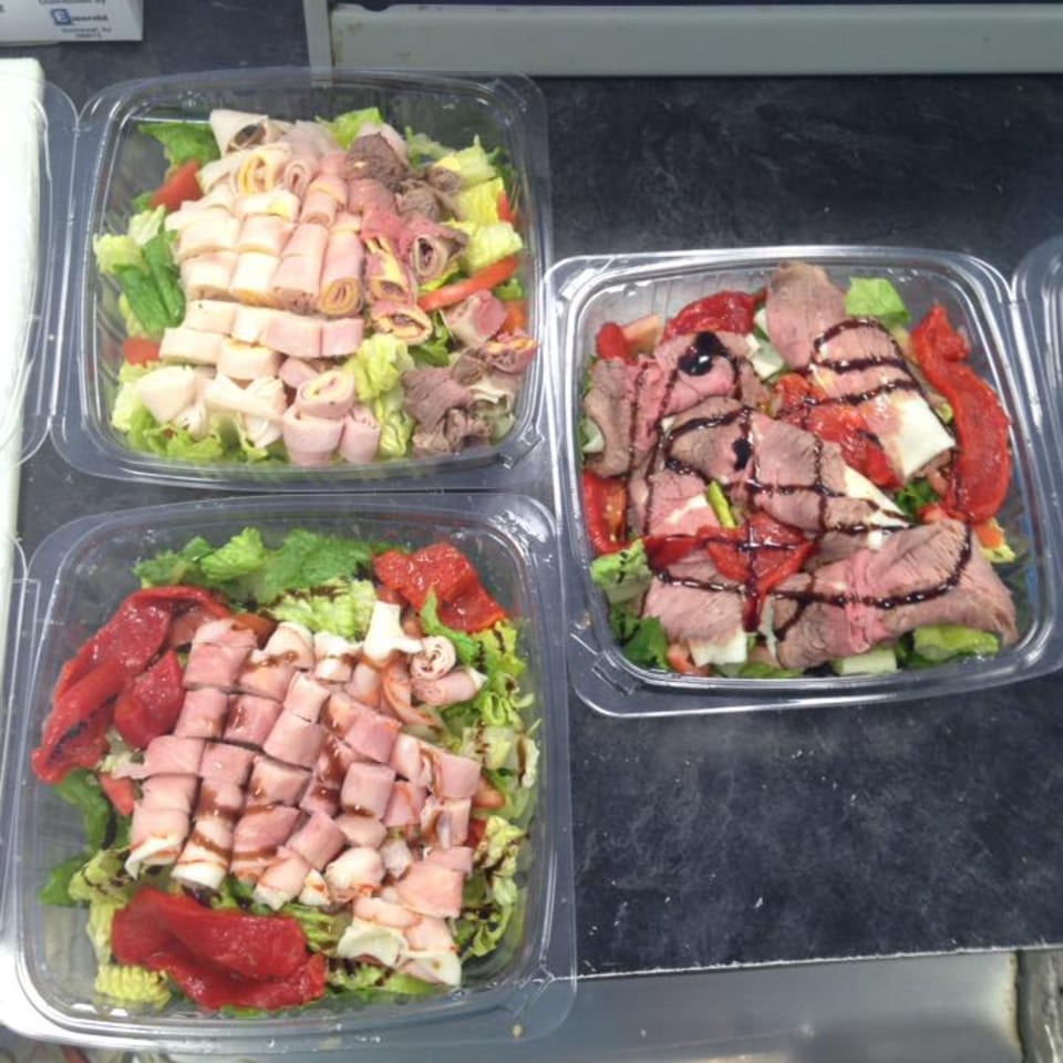 Three deli salads in clear plastic containers, featuring meats, lettuce, and roasted red peppers.