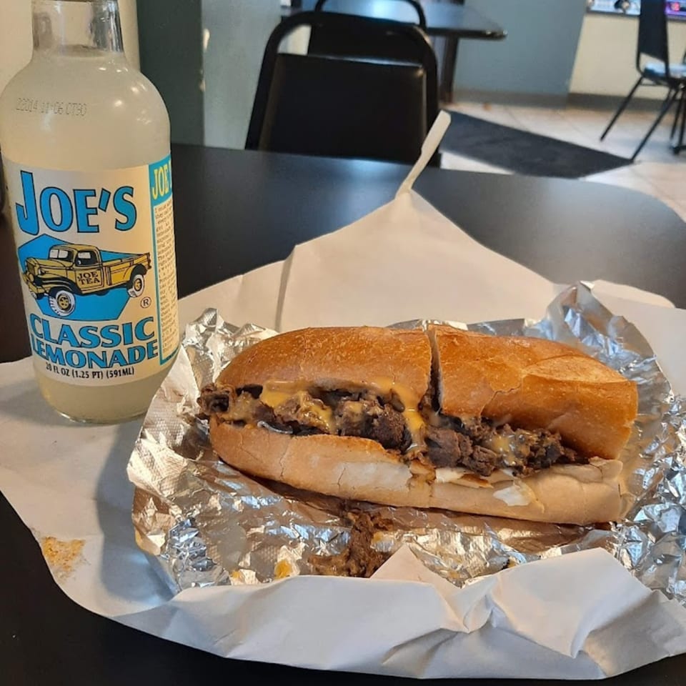 A Bing's Beach House Deli cheesesteak sandwich in foil next to a bottle of Joe's Classic Lemonade.