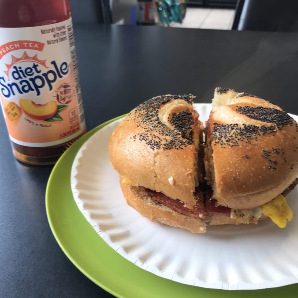 Poppy seed bagel sandwich with meat and egg, next to a bottle of Diet Snapple Peach Tea.